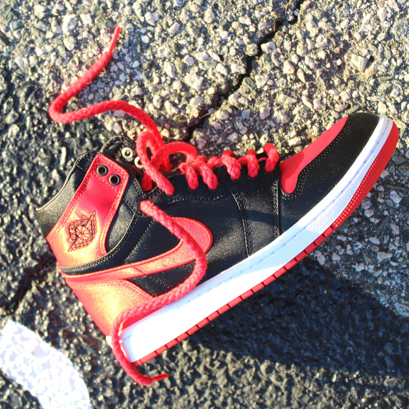 Looped Laces Red Rope Shoelaces tied in a single Air Jordan 1 High Satin Bred Toe sneaker laying on its side on cement