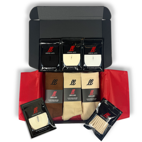 Looped Laces black gift box containing crew socks in chocolate brown, sand beige and light cream with black, white, and cream flat laces, and cream waxed laces and natural color rope laces, all on top of red tissue paper